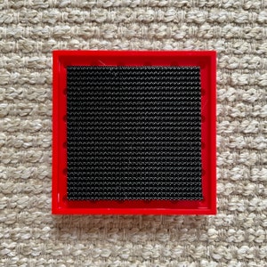 May include: A red square frame with a black mesh insert. The frame is made of plastic and has a smooth surface.