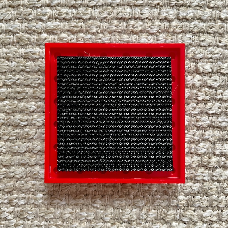 May include: A red square frame with a black mesh insert. The frame is made of plastic and has a smooth surface.