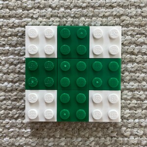 May include: A 3x3 grid of LEGO bricks, with alternating white and green bricks. The bricks have the word "LEGO" printed on them.