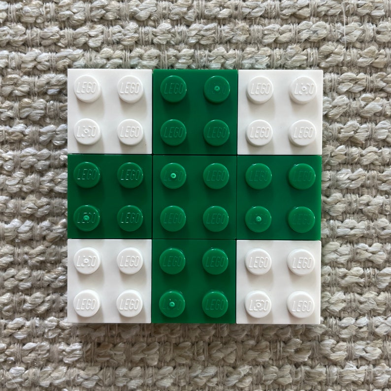 May include: A 3x3 grid of LEGO bricks, with alternating white and green bricks. The bricks have the word "LEGO" printed on them.
