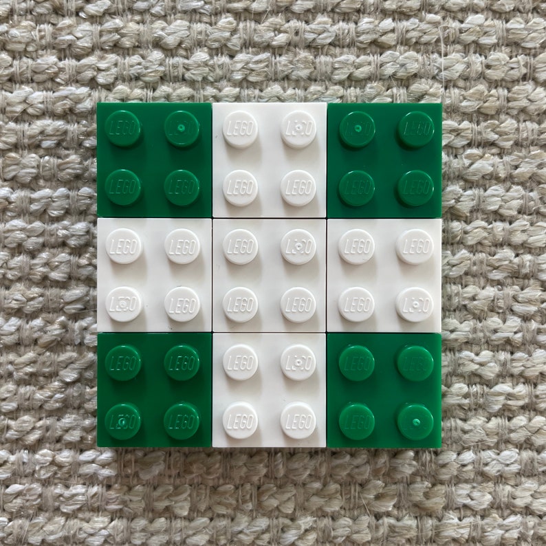 May include: A 3x3 grid of LEGO bricks, alternating between green and white. Each brick has the word "LEGO" printed on it.