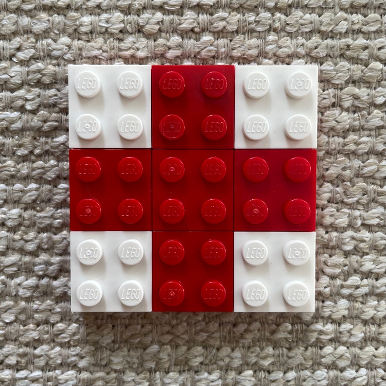 May include: A 3x3 grid of LEGO bricks, with the centre square made up of nine red bricks and the surrounding squares made up of nine white bricks. Each brick has the word "LEGO" printed on it.