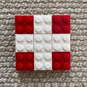 May include: A 3x3 grid of LEGO bricks, with alternating red and white bricks. The bricks have the word "LEGO" printed on them.