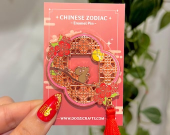 Könnte beinhalten: Eine rosa Emaille-Anstecknadel mit einer Comic-Maus in einem roten und goldenen Gitterrahmen mit einem roten Quasten. Die Anstecknadel ist ein Tier des chinesischen Tierkreises und trägt die Aufschrift "Chinesisches Tierkreiszeichen - Emaille-Anstecknadel - www.doozicrafts.com".