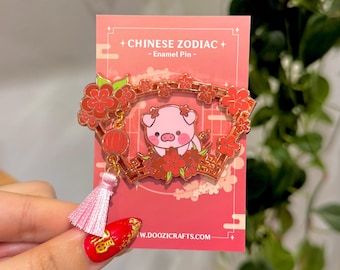 Könnte beinhalten: Ein rosa Emaille-Pin mit einem Schwein, umgeben von roten Blumen und einem goldenen Rahmen. Der Pin hat einen rosa Quastenanhänger und einen roten Laternenanhänger. Die Rückseite trägt die Aufschrift "+ CHINESE ZODIAC + - Enamel Pin -" und die Website-Adresse www.doozicrafts.com.