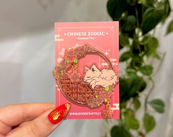 Könnte beinhalten: Ein rosafarbener Emaille-Pin mit einem schlafenden Fuchs in einem dekorativen Kreis mit floralen Akzenten. Der Pin trägt die Aufschrift "+ CHINESE ZODIAC + - Enamel Pin -" und die Website-Adresse www.doozi.crafts.co.