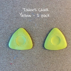 May include: Two yellow tailor's chalk triangles, each with a round center, labeled "Tailor's Chalk Yellow - 2 pack".