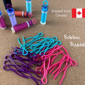 May include: A pile of colourful plastic bobbin buddies in pink, purple, and turquoise. The bobbin buddies are used to hold yarn or thread on a sewing machine.