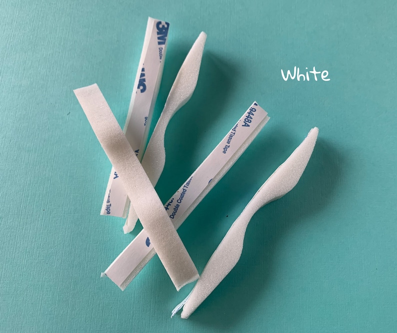 Peut inclure: Quatre bandes de mousse blanche avec un dos adh&eacute;sif. Les bandes sont courb&eacute;es et portent l'inscription "Double Coated Tape" et "9448A". Le texte "White" est &eacute;crit en blanc sur un fond turquoise.