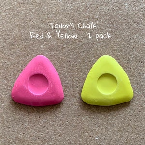 May include: Two triangular tailor's chalk pieces, one red and one yellow, with a round hole in the center. "Tailor's Chalk Red & Yellow - 2 pack" is written above the chalk.