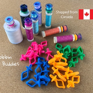 May include: A collection of colorful bobbin buddies in pink, blue, green, and orange. The bobbin buddies are small plastic devices used to hold and organize sewing machine bobbins. The image also shows spools of thread in various colors.