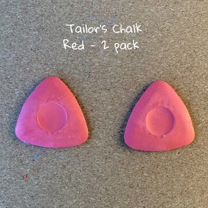 May include: Two red tailor's chalk triangles, each with a round hole in the center. The text "Tailor's Chalk Red - 2 pack" is written above the chalk.