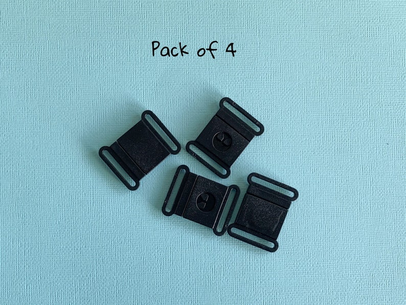 Pu&ograve; includere: Quattro fibbie a sgancio laterale in plastica nera su sfondo azzurro. Ogni fibbia ha una forma rettangolare con un design curvo e un meccanismo di rilascio centrale. Il testo "Pack of 4" si trova nell'angolo in alto a sinistra.