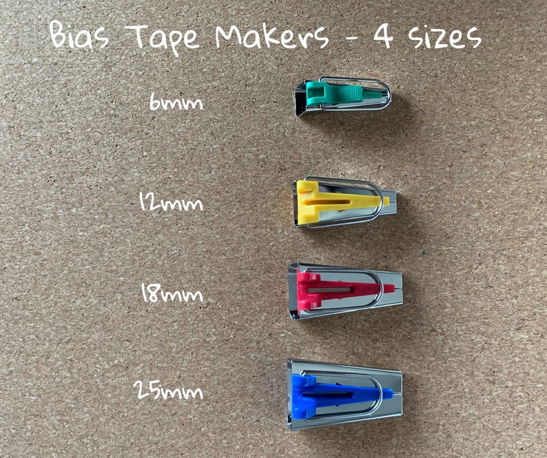 K&ouml;nnte beinhalten: Vier Schr&auml;gbandmacher in verschiedenen Gr&ouml;&szlig;en: 6 mm, 12 mm, 18 mm und 25 mm. Die Schr&auml;gbandmacher sind aus Metall und haben einen Kunststoffgriff. Die Griffe sind gr&uuml;n, gelb, rot und blau.