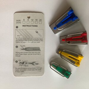 K&ouml;nnte beinhalten: Ein Satz von vier Schr&auml;gband-Herstellern in verschiedenen Farben: Blau, Rot, Gelb und Gr&uuml;n. Die Schr&auml;gband-Hersteller werden verwendet, um Schr&auml;gband f&uuml;r N&auml;hprojekte zu erstellen. Das Bild enth&auml;lt auch Anweisungen zur Verwendung der Schr&auml;gband-Hersteller.