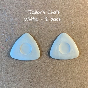 May include: Two white triangular tailor's chalk pieces with a round hole in the center.  The text "Tailor's Chalk White - 2 pack" is written above the chalk.