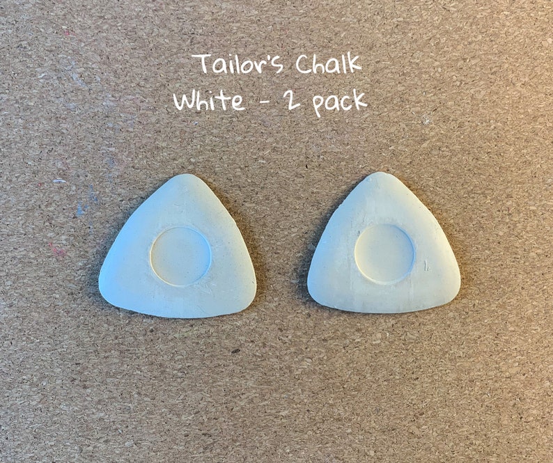 May include: Two white triangular tailor's chalk pieces with a round hole in the center.  The text "Tailor's Chalk White - 2 pack" is written above the chalk.