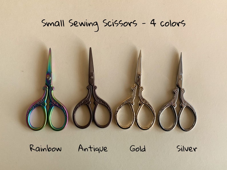 May include: Four pairs of small sewing scissors with ornate handles. The scissors are rainbow, antique, gold, and silver.