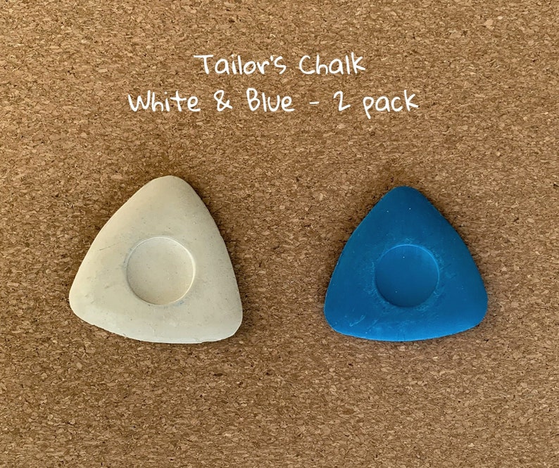 May include: Two tailor's chalk pieces, one white and one blue, in the shape of a triangle with a round hole in the center. "Tailor's Chalk White & Blue - 2 pack" is written above the chalk.