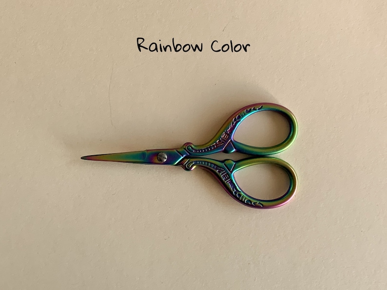 May include: Rainbow colored metal scissors with an ornate design. The scissors have a small screw in the center.