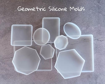 May include: A set of nine white silicone molds in various geometric shapes, including circles, squares, octagons, and rectangles. The molds are arranged on a gray textured surface. Geometric Silicone Molds.