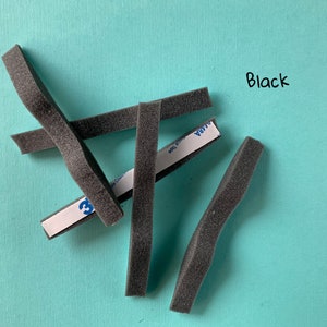 Peut inclure: Cinq bandes de mousse noires avec un dos adh&eacute;sif. Les bandes sont courb&eacute;es et ont une surface textur&eacute;e. Le texte "Black" est &eacute;crit &agrave; l'encre noire sur un fond turquoise.