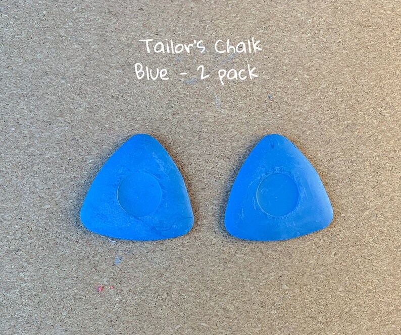 May include: Two blue tailor's chalk triangles, each with a round center, on a brown background. The text "Tailor's Chalk Blue - 2 Pack" is written in white above the chalk.