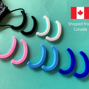 May include: A set of 10 silicone ear savers in black, white, pink, light blue, and blue. The ear savers are designed to help keep face masks from pulling on the ears.