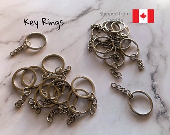 May include: A collection of silver-colored key rings with chain attachments, displayed on a marble-patterned surface. The text "Key Rings" is written in black script. The key rings are of various sizes and shapes.