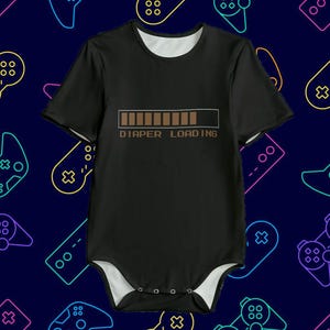 May include: Black baby bodysuit with white trim and short sleeves. It has a brown loading bar graphic and the text "DIAPER LOADING". The background is dark blue with neon video game controller outlines.