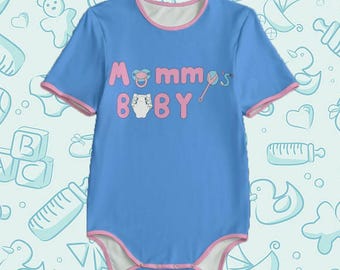 Può includere: Un body da bambino azzurro con maniche corte e bordi rosa. Il testo "Mommy's Baby" è stampato in rosa sul davanti, insieme a un'immagine di ciuccio e pannolino. Il body è progettato per neonati.