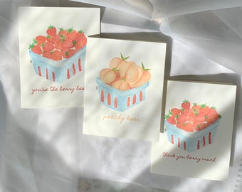 Pode incluir: Três cartões de felicitações em aquarela com ilustrações de frutas. Um cartão mostra morangos em uma cesta azul com o texto "you're the berry best". Outro mostra pêssegos com o texto "peachy keen". O terceiro cartão mostra morangos com o texto "thank you berry much."