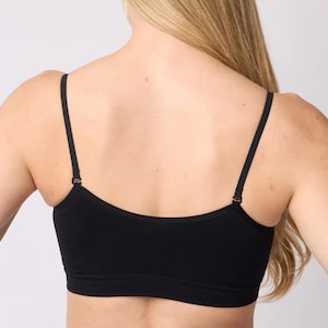 Op de afbeelding: Een effen zwarte crop top met een ronde halslijn en dunne, verstelbare schouderbandjes. Het kledingstuk heeft een eenvoudig, naadloos ontwerp dat de bovenrug en borst bedekt, wat zorgt voor een strakke en eenvoudige uitstraling.