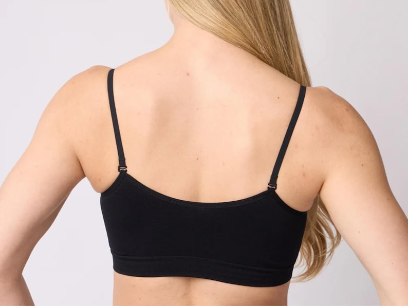 Op de afbeelding: Een effen zwarte crop top met een ronde halslijn en dunne, verstelbare schouderbandjes. Het kledingstuk heeft een eenvoudig, naadloos ontwerp dat de bovenrug en borst bedekt, wat zorgt voor een strakke en eenvoudige uitstraling.