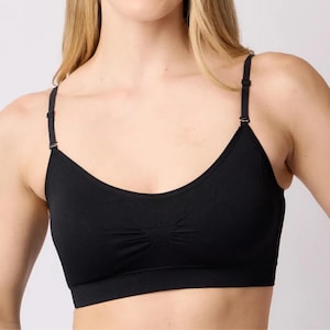 Op de afbeelding: Een effen zwarte bralette met een ronde halslijn, dunne verstelbare schouderbandjes met metalen schuifjes en een subtiel geplooid detail in het midden van de borst. Het kledingstuk heeft een brede, platte elastische band aan de onderkant.