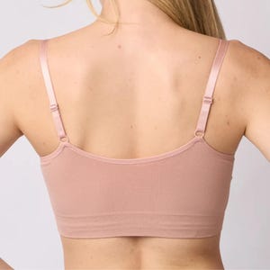 Op de afbeelding: Een naadloze bralette in oudroze met een diepe ruguitsnijding, dunne verstelbare schouderbandjes met bijpassende metalen schuifjes en een brede, geribbelde onderband die zorgt voor een nauwsluitende pasvorm rond het bovenlichaam.