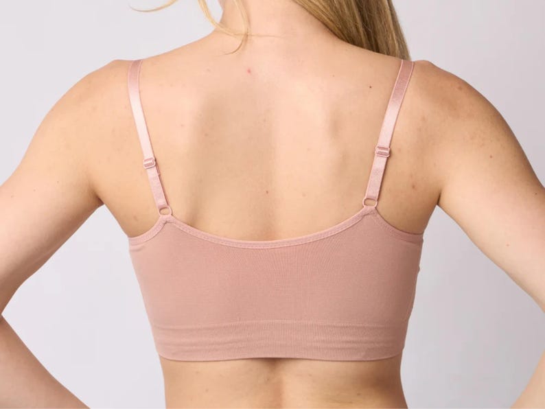 Op de afbeelding: Een naadloze bralette in oudroze met een diepe ruguitsnijding, dunne verstelbare schouderbandjes met bijpassende metalen schuifjes en een brede, geribbelde onderband die zorgt voor een nauwsluitende pasvorm rond het bovenlichaam.