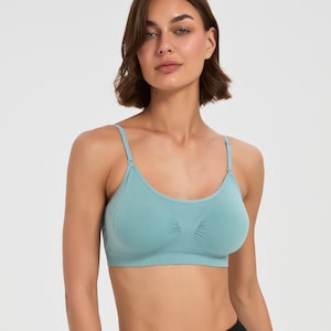 Op de afbeelding: Een naadloze bralette in lichtblauwgroen met een ronde halslijn, dunne verstelbare schouderbandjes en een brede band onder de buste. De stof heeft een gladde, matte textuur met subtiele geribbelde details in het midden tussen de cups.