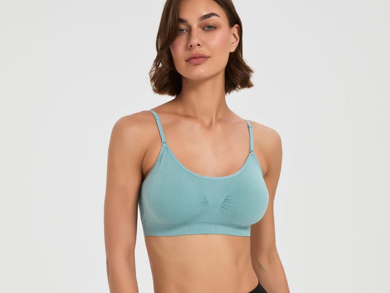 Op de afbeelding: Een naadloze bralette in lichtblauwgroen met een ronde halslijn, dunne verstelbare schouderbandjes en een brede band onder de buste. De stof heeft een gladde, matte textuur met subtiele geribbelde details in het midden tussen de cups.