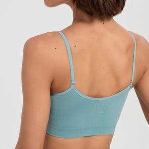 Op de afbeelding: Een lichtblauwe naadloze bralette met dunne, verstelbare schouderbandjes en een brede, geribbelde onderband. Het kledingstuk heeft een diepe ruguitsnijding en is gemaakt van een effen, gestructureerde stof die zorgt voor een nauwsluitende pasvorm.