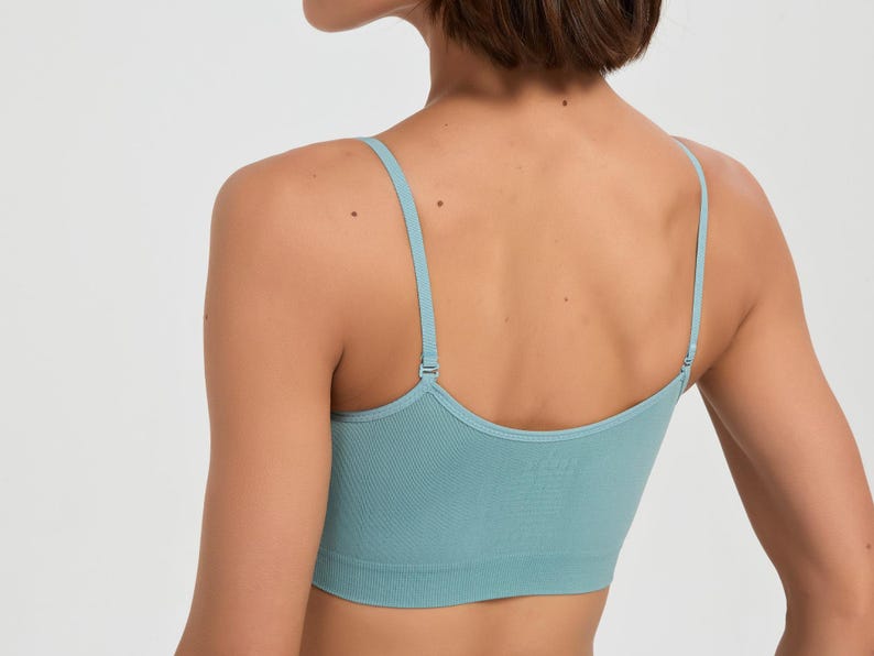 Op de afbeelding: Een lichtblauwe naadloze bralette met dunne, verstelbare schouderbandjes en een brede, geribbelde onderband. Het kledingstuk heeft een diepe ruguitsnijding en is gemaakt van een effen, gestructureerde stof die zorgt voor een nauwsluitende pasvorm.