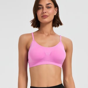 May include: A bright pink seamless bralette featuring a scoop neckline, thin adjustable shoulder straps with metal sliders, and a wide ribbed underband. The garment is constructed from a solid-colored, flexible fabric with a textured center panel.
