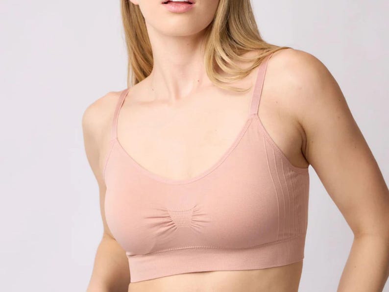 Op de afbeelding: Een naadloze bralette in een lichte perzikkleur met een ronde halslijn, dunne verstelbare schouderbandjes en een geribbelde textuur onder de buste. Het kledingstuk heeft een geplooid detail in het midden van de borst en een brede steunband.