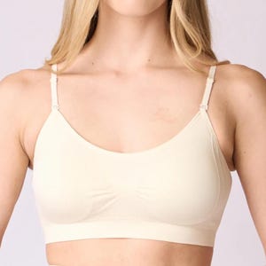 Op de afbeelding: Een naadloze, cr&egrave;mekleurige bralette met een ronde halslijn, een brede band onder de buste en dunne, verstelbare schouderbandjes. Het kledingstuk is gemaakt van een gladde, effen stof met subtiele geribbelde details in het midden.