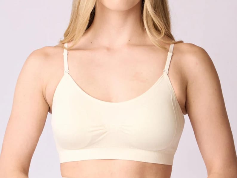 Op de afbeelding: Een naadloze, cr&egrave;mekleurige bralette met een ronde halslijn, een brede band onder de buste en dunne, verstelbare schouderbandjes. Het kledingstuk is gemaakt van een gladde, effen stof met subtiele geribbelde details in het midden.