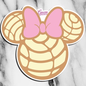 May include: A sticker featuring a cartoon character with a pink bow and ears shaped like a traditional Mexican sweet bread, "pan dulce". The text "CORAZON CORAZONCITO" is visible on the bow.