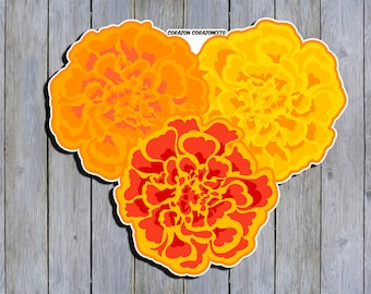 Puede incluir: Tres flores de cempasúchil en tonos naranja y rojo, dispuestas en forma de corazón. Las flores están sobre un fondo de madera. El texto "CORAZON CORAZONCITO" está en la parte superior de la imagen.