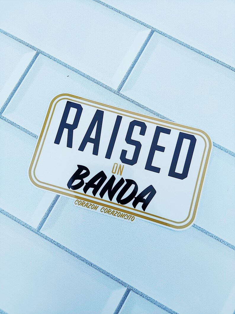 May include: A white sticker with gold trim and black text that reads "RAISED ON BANDA" with the words "CORAZON CORAZONCITO" below.