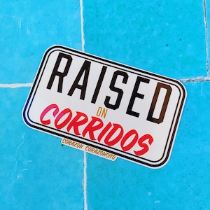 May include: White sticker with black border and text "RAISED ON CORRIDOS" in black and red. The text "CORAZON CORAZONCITO" is in gold below the main text.