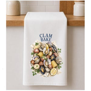 May include: White kitchen towel with a watercolour illustration of a clam bake. The design features clams, corn, potatoes, and lemons on parchment paper, with the words "CLAM BAKE" in blue.